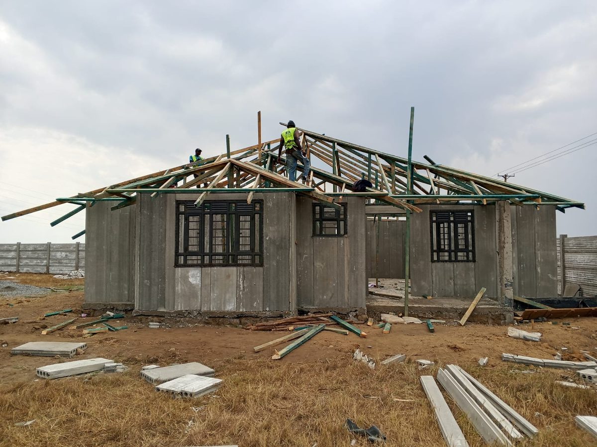 Precast panel bungalow with roof truss installation in progress, crew on site